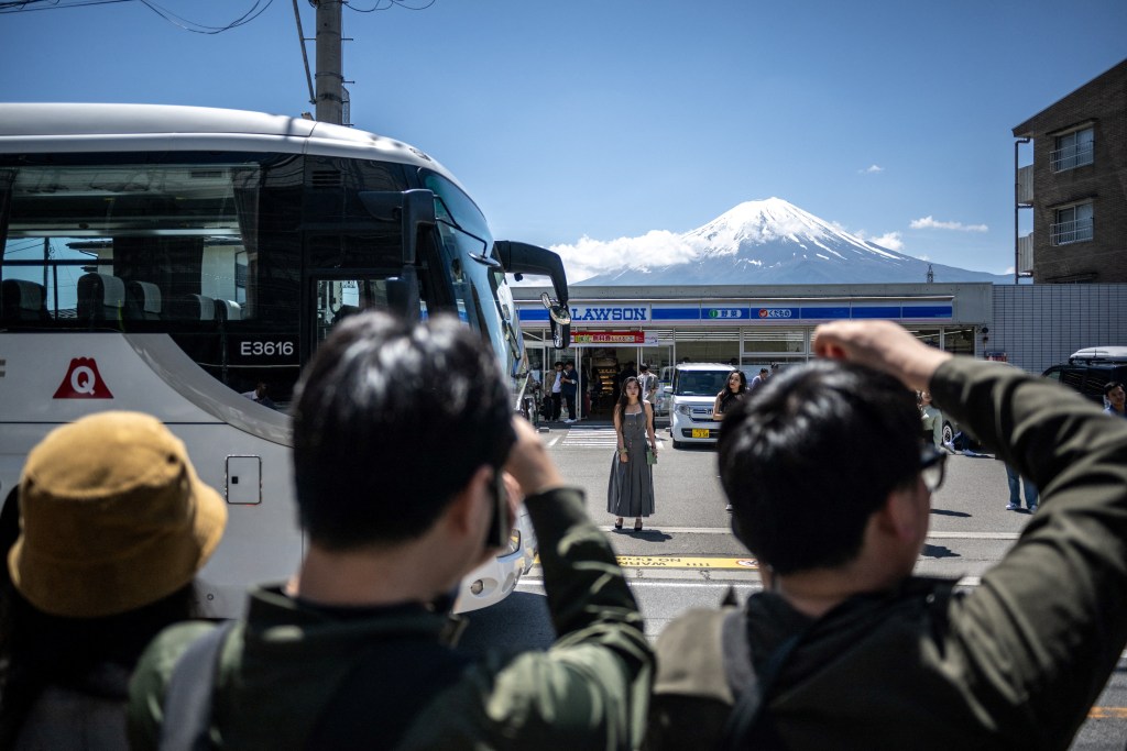 Tourists take pictures from the opposite street of a convenience store with Mount Fuji on May 3, 2024, before a huge black barrier which will be installed to block Mount Fuji from view, in the town of Fujikawaguchiko, Yamanashi prefecture. 