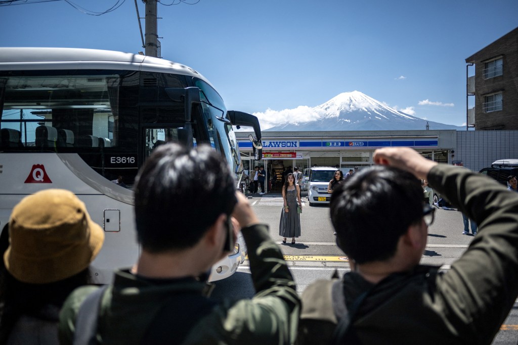 Tourists take pictures from the opposite street of a convenience store with Mount Fuji on May 3, 2024, before a huge black barrier which will be installed to block Mount Fuji from view, in the town of Fujikawaguchiko, Yamanashi prefecture.