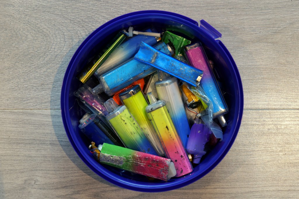 A collection of discarded electronic cigarette vapes stored in a dark blue plastic tub