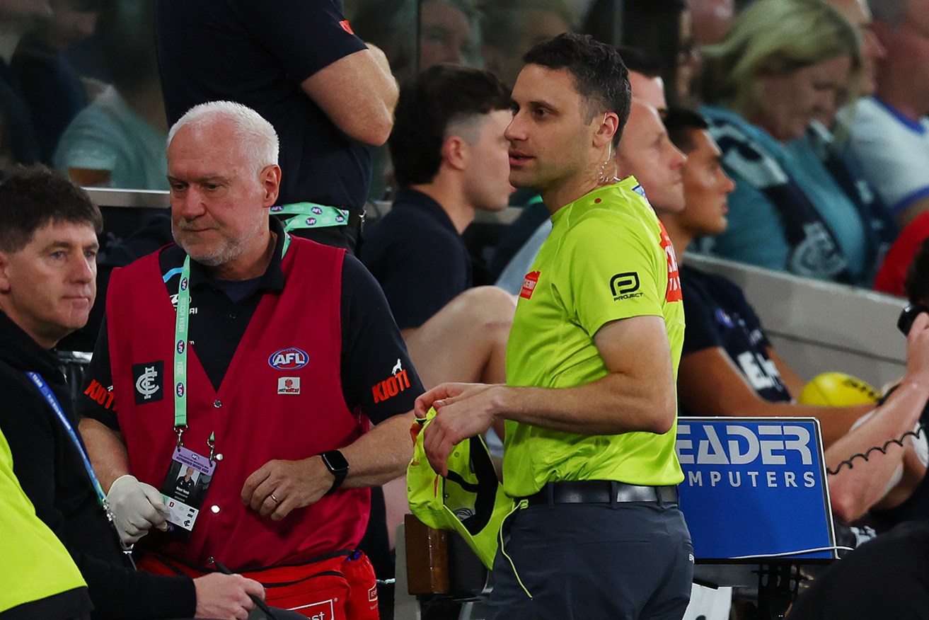 AFL goal umpire Steven Piperno seeks medical attention after being hit in the head by a bottle on Sunday.