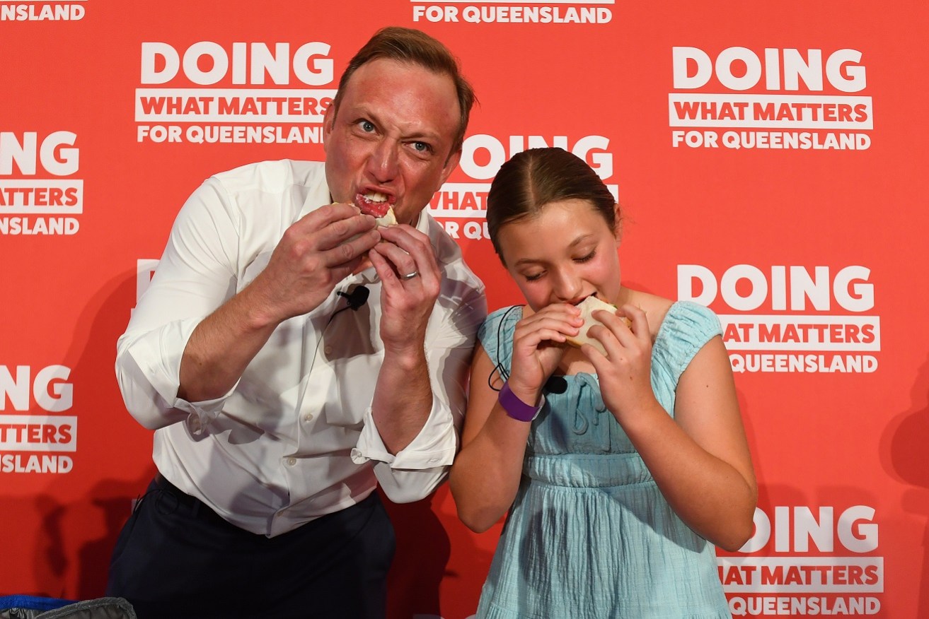 Queensland Premier Steven Miles eats a sausage sandwich with daughter Bridie.